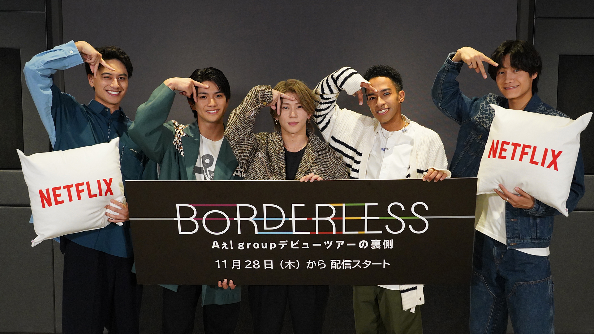 Five members of the Ae! group pose together, holding a sign that reads 'BORDERLESS' and cushions with the Netflix logo, showcasing their playful spirit during a promotional event.