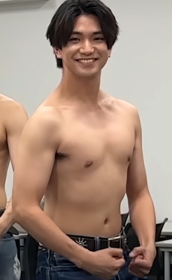 Yoshinori Masakado smiling confidently with a sculpted physique, wearing simply a belt and jeans, showcasing his fitness journey.