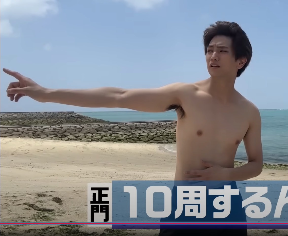 A shirtless male figure standing on a beach, gesturing with one arm raised while looking at the distance, with a serene ocean backdrop.
