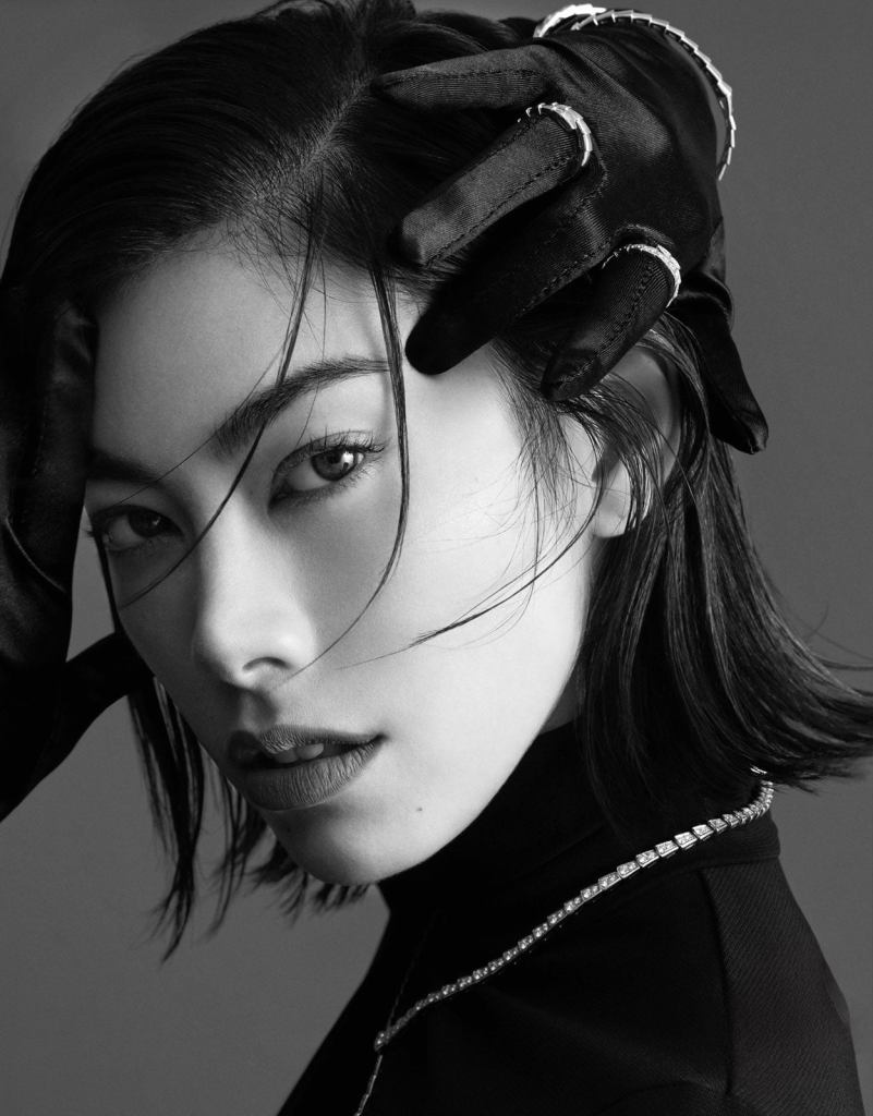 Black and white portrait of a model with a stylish hairstyle, wearing a black turtleneck and gloves, showcasing a confident expression.
