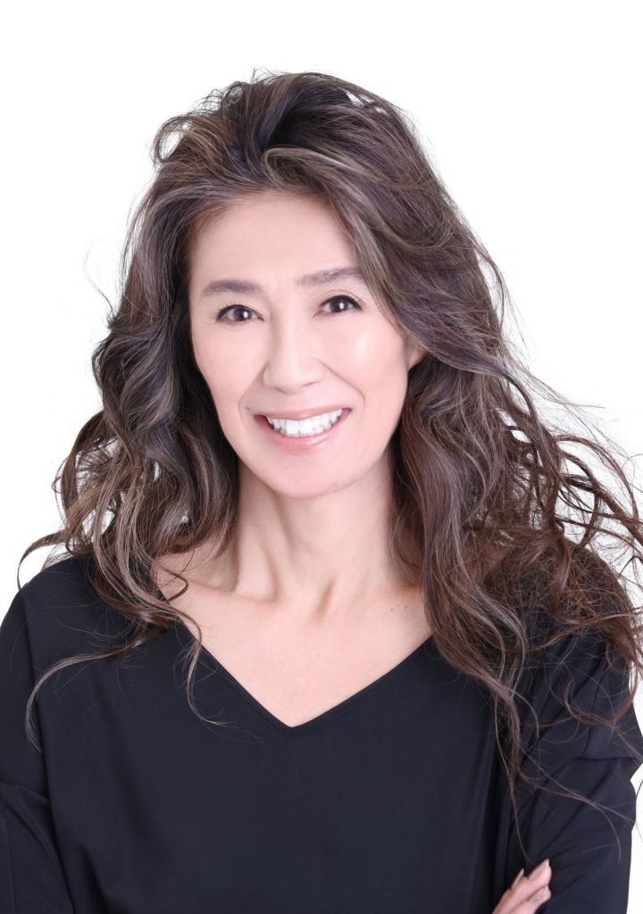 Portrait of a woman with long wavy hair, smiling while wearing a black top against a white background.