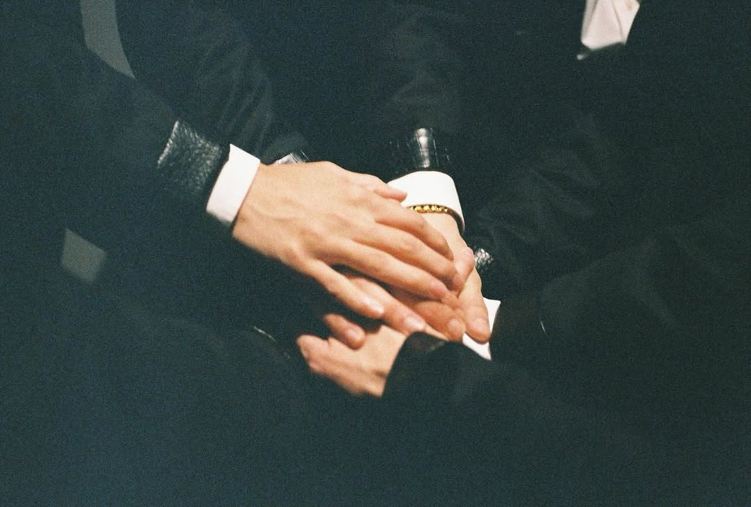 A close-up of several hands resting on top of each other, showcasing a sense of unity and connection, with members dressed in black attire.