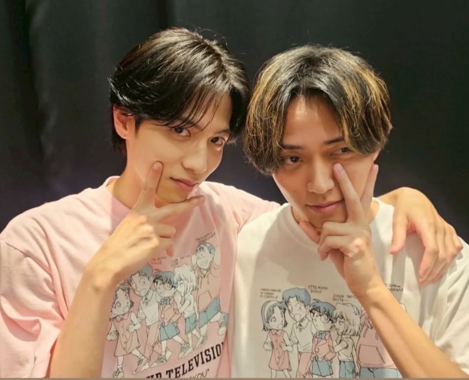 Two male individuals posing for the camera, wearing matching t-shirts featuring a cartoon illustration, with playful expressions and hand gestures.