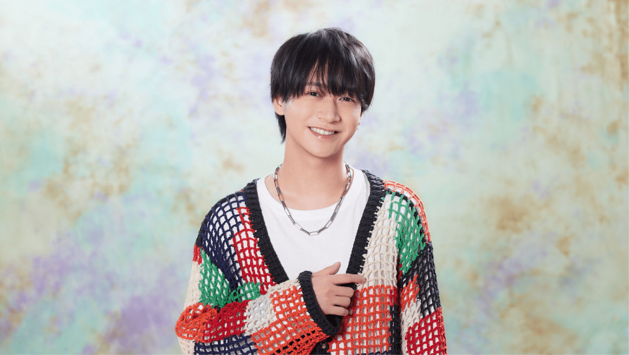 Naoki Fujii, wearing a colorful knitted sweater, smiles warmly against a soft, pastel background, symbolizing his transition to a solo artist.