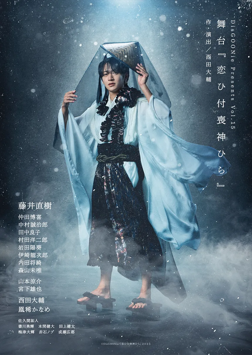 A young male performer dressed in a traditional, flowing kimono-like outfit stands dramatically in a misty setting, holding a veil over his head, evoking a mystical ambiance.