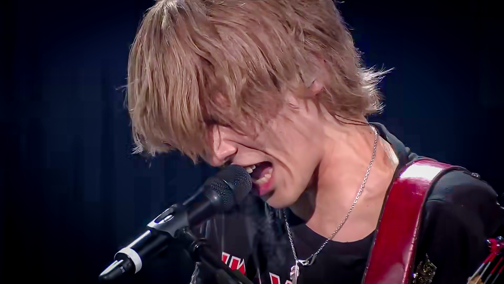 A performer passionately singing into a microphone with long, messy hair during a live music performance.