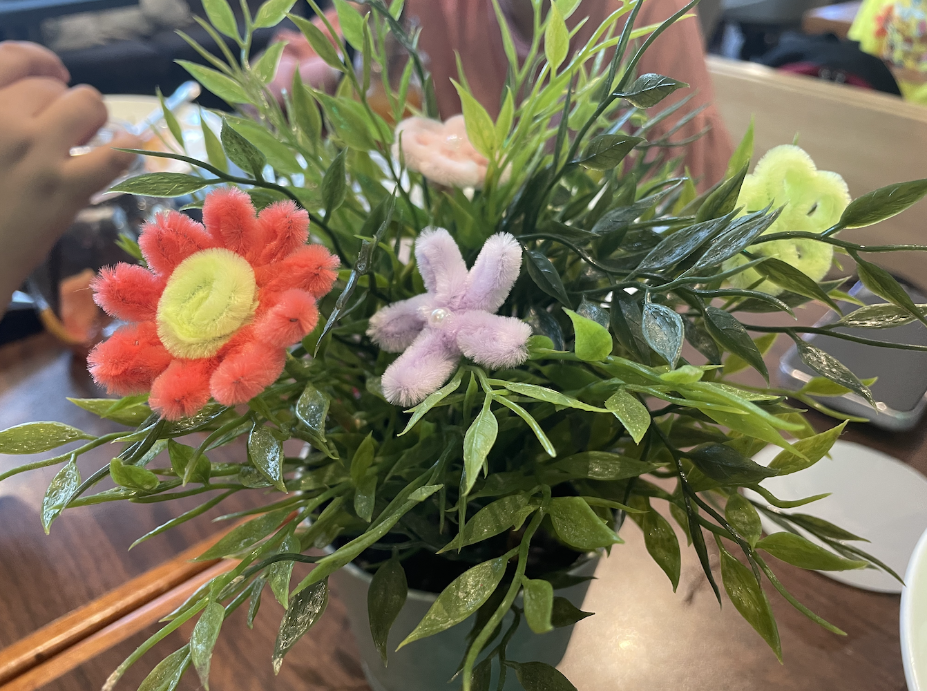 A close-up view of a decorative potted plant featuring colorful pom-pom flowers in shades of pink, red, and green, surrounded by lush green leaves.