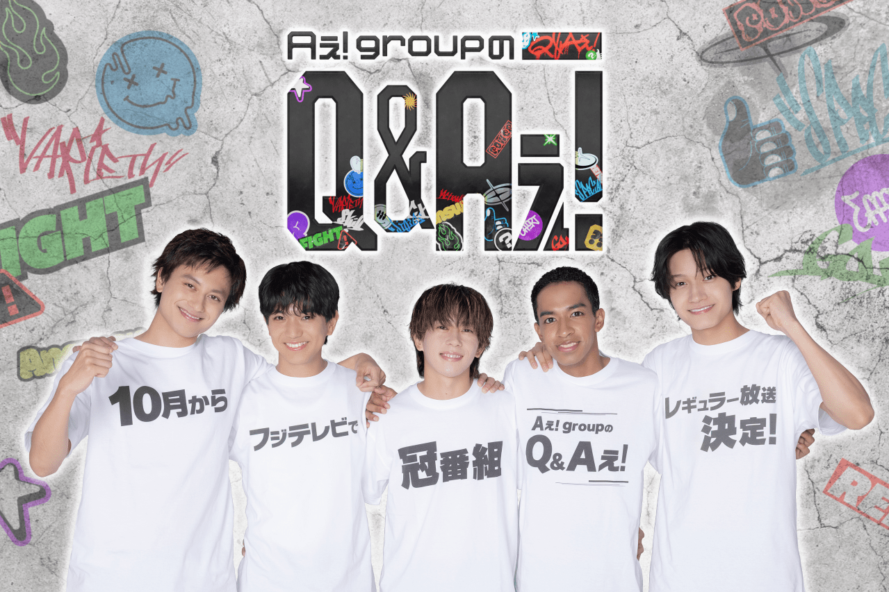 Group of five members from Ae! group posing together, wearing matching white shirts with various Japanese text phrases related to their upcoming variety show, set against a colorful graffiti-style background.