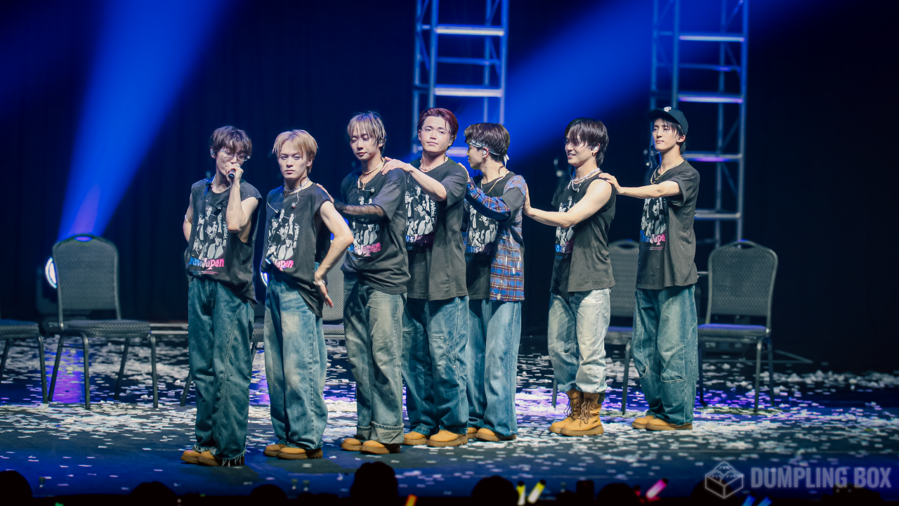 Seven members of Travis Japan performing on stage, wearing matching outfits and surrounded by a colorful stage setup.