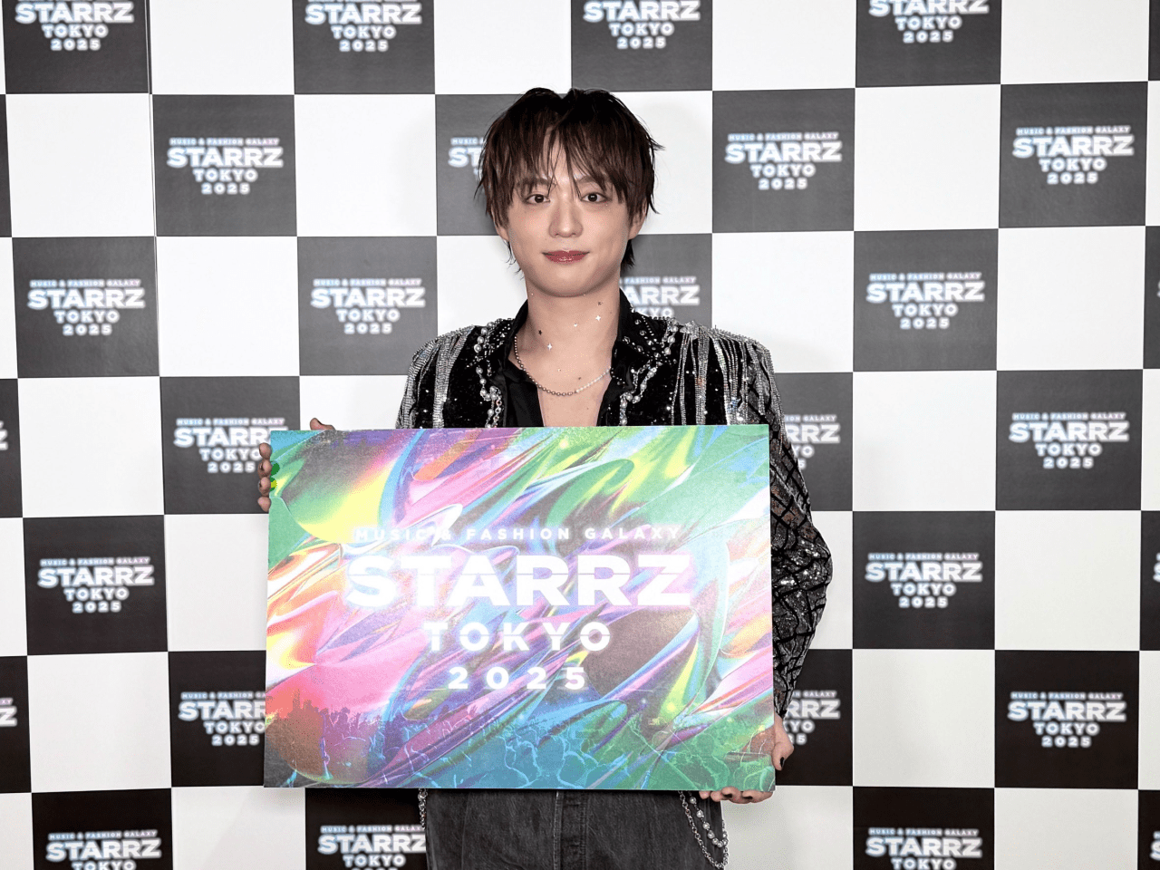 Taisei Fukumoto holding a promotional sign for STARRZ TOKYO 2025 in front of a patterned background featuring the event's logo.
