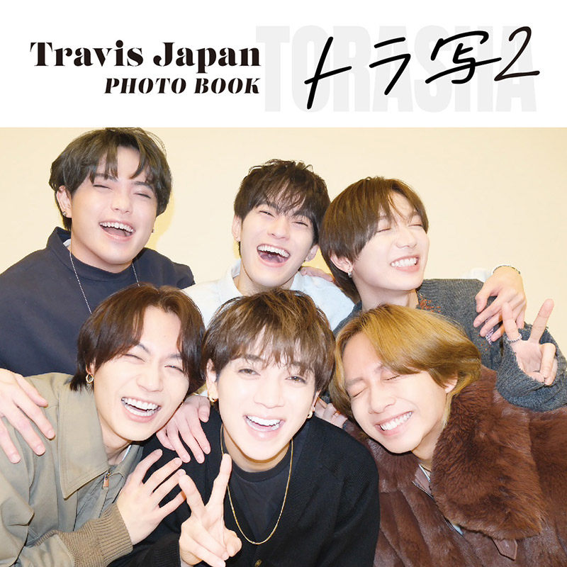 A joyful group photo of six members of Travis Japan smiling and posing together, promoting their photo book titled 'トラ写2'.