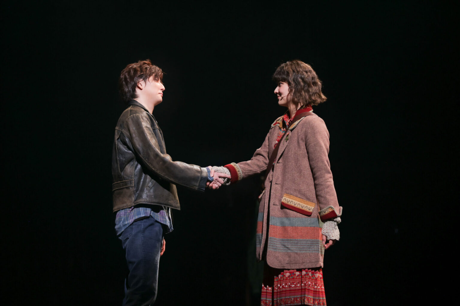 A scene from the musical 'Once', featuring two characters, Guy and Girl, who are shaking hands on stage, with a dark background.