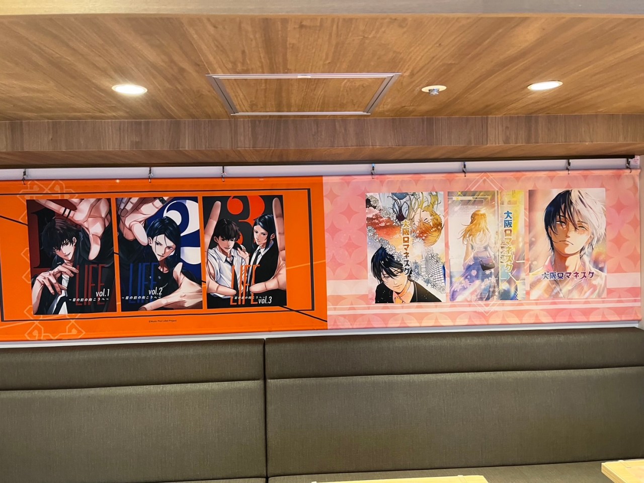 Posters of comic volumes displayed on the wall of the Super Comics Cafe, featuring characters from SUPER EIGHT's songs and comics.
