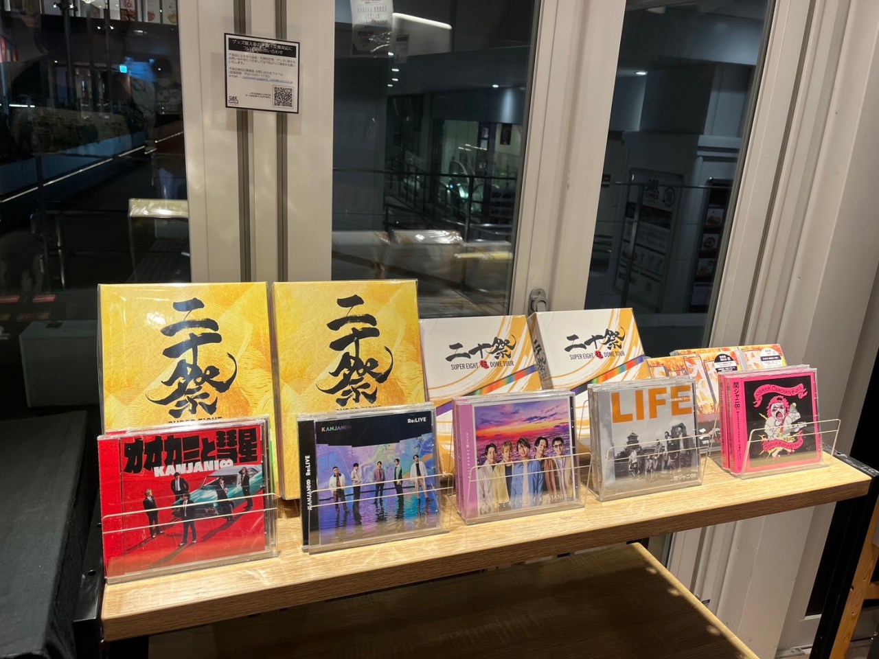 A display of music CDs and merchandise related to SUPER EIGHT and Kanjani, set on a wooden shelf in a cafe, with a bright, inviting ambiance.