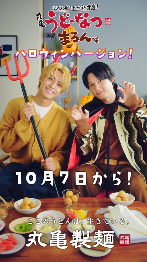 Kaito Takahashi and Hokuto Matsumura dressed in Halloween costumes, posing with a red pitchfork and smiling, surrounded by various food items related to Marugame Udon.