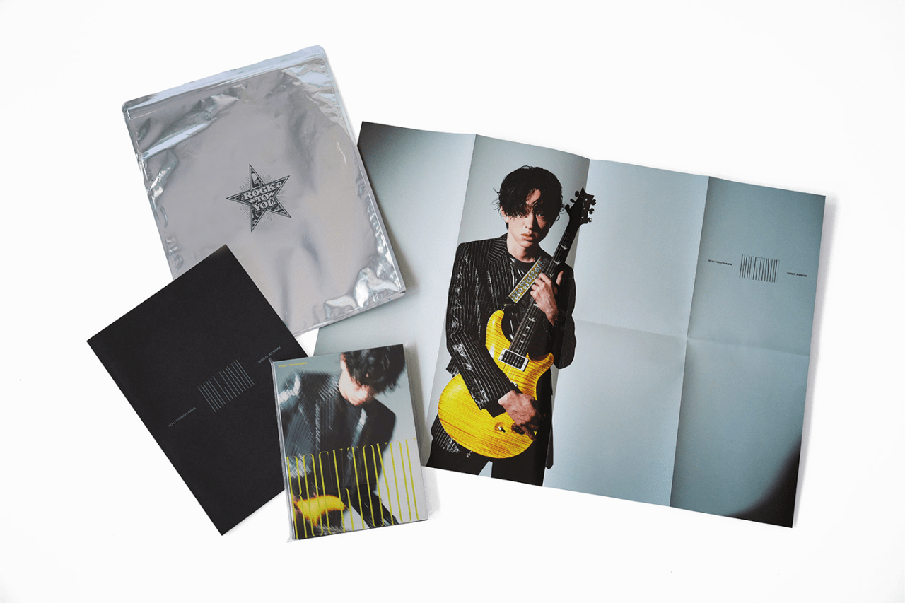 A collection of promotional items for You Yokoyama's 'ROCK TO YOU' including a silver bag, photo book, and a CD featuring the artist with a yellow guitar.