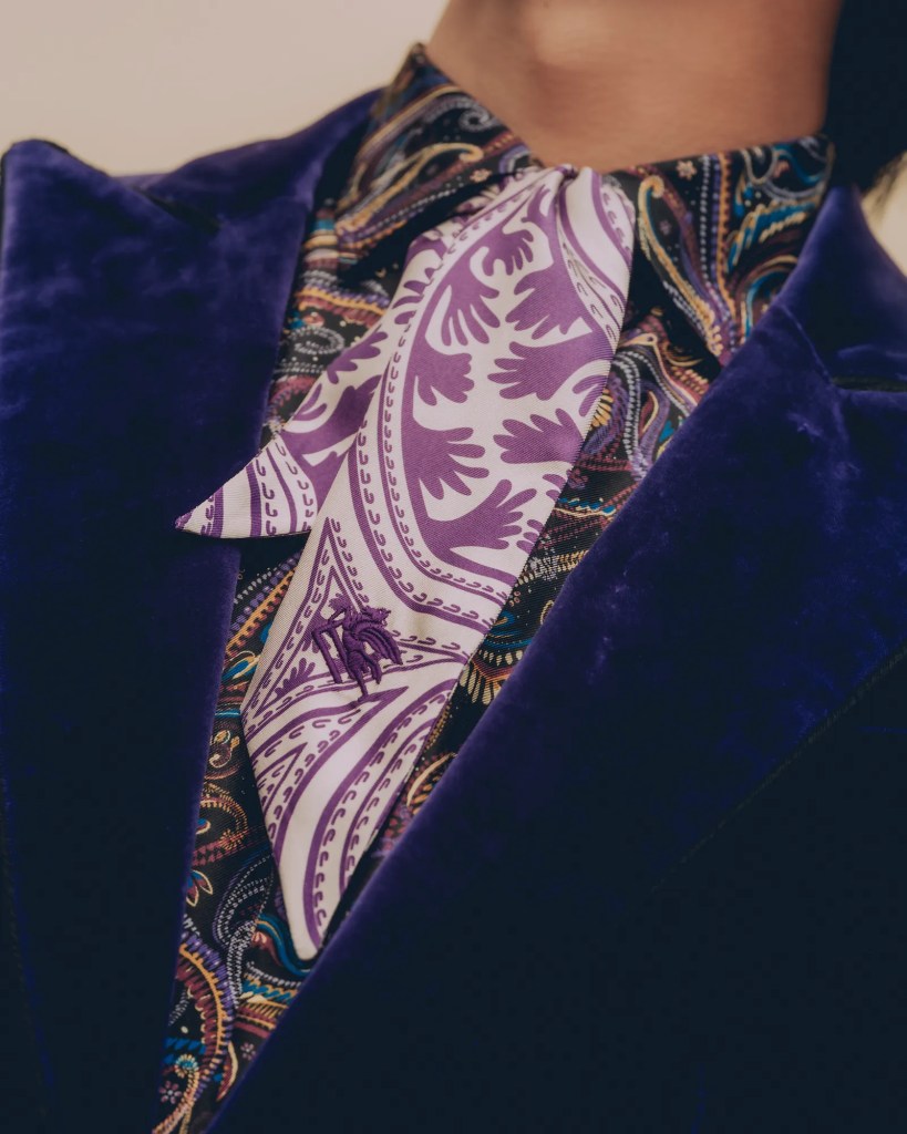 Close-up of a model's upper body wearing a velvet jacket and a patterned shirt featuring a purple paisley scarf, showcasing intricate details and textures.