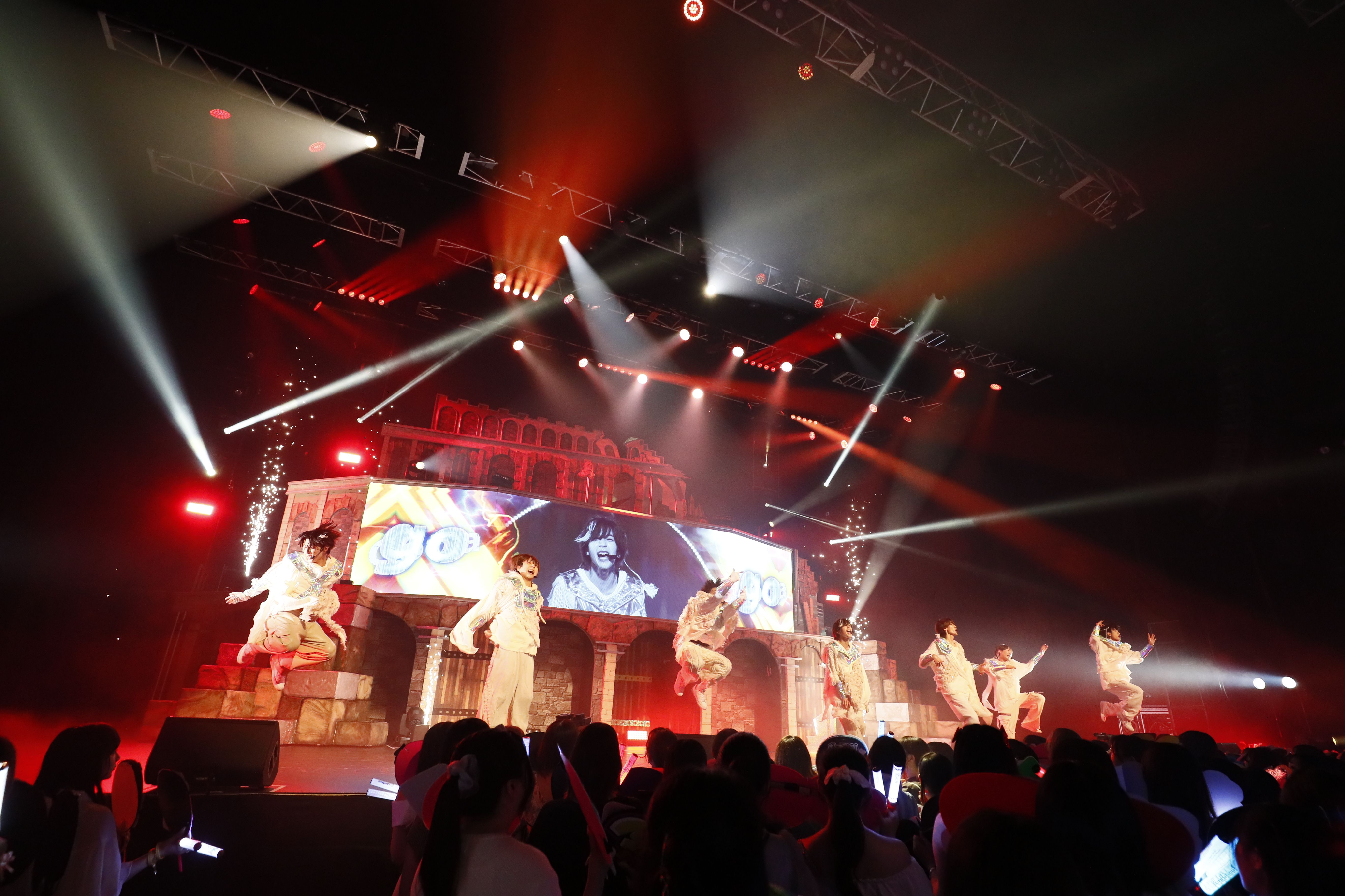 A lively performance by the Kansai group AmBitious at Kanadevia Hall, featuring dynamic choreography, colorful stage lighting, and enthusiastic fans in the audience.