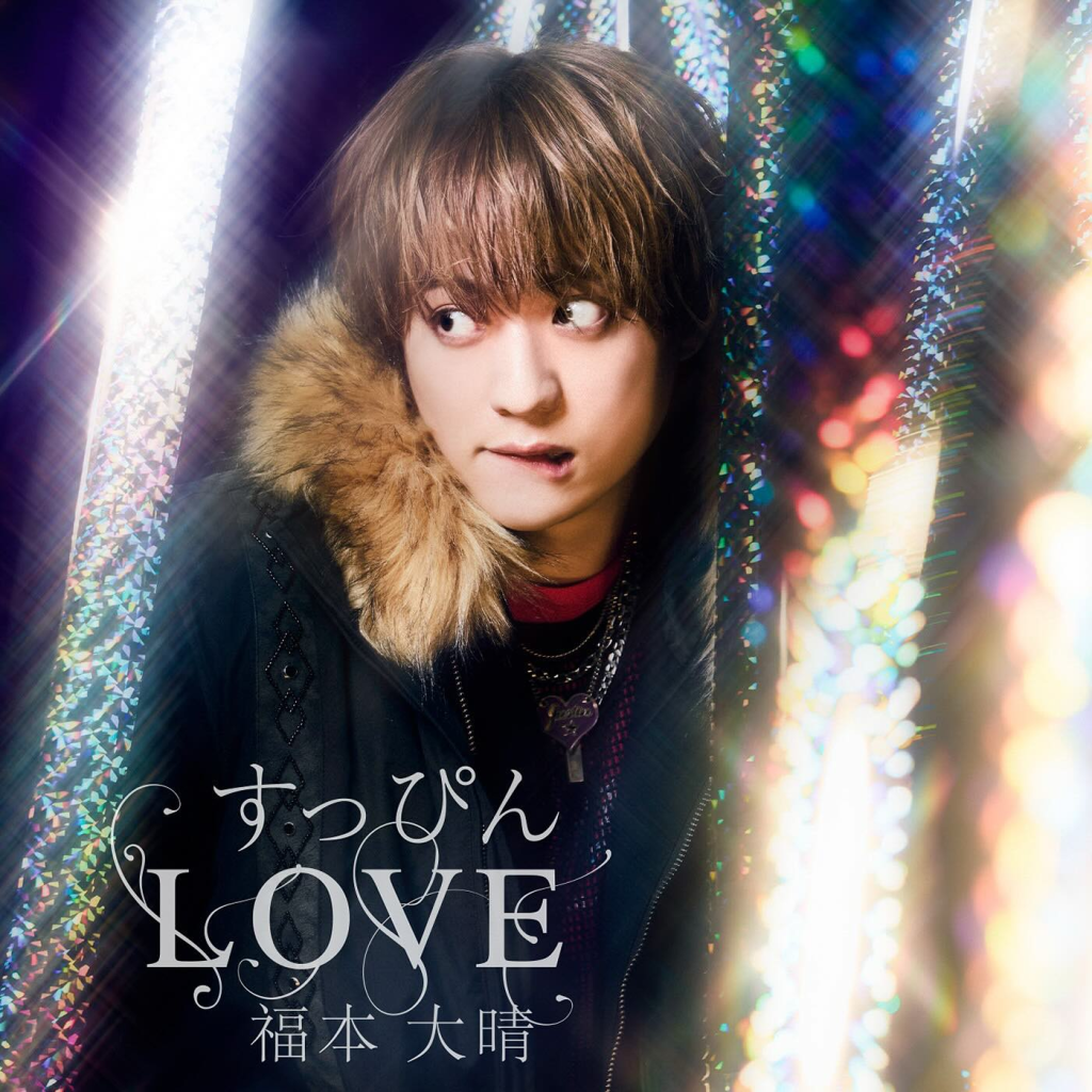 A young male artist with tousled hair and wearing a furry hooded jacket gazes sideways with a playful expression, surrounded by colorful sparkling lights. The text 'すっぴん LOVE' is prominently displayed at the bottom.
