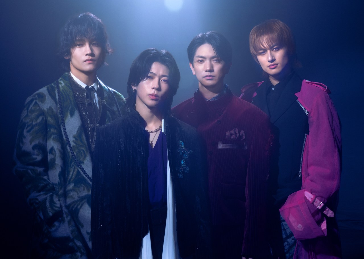 Four individuals posing together in dramatic lighting, wearing stylish and ornate outfits, exuding a sense of confidence and artistry.