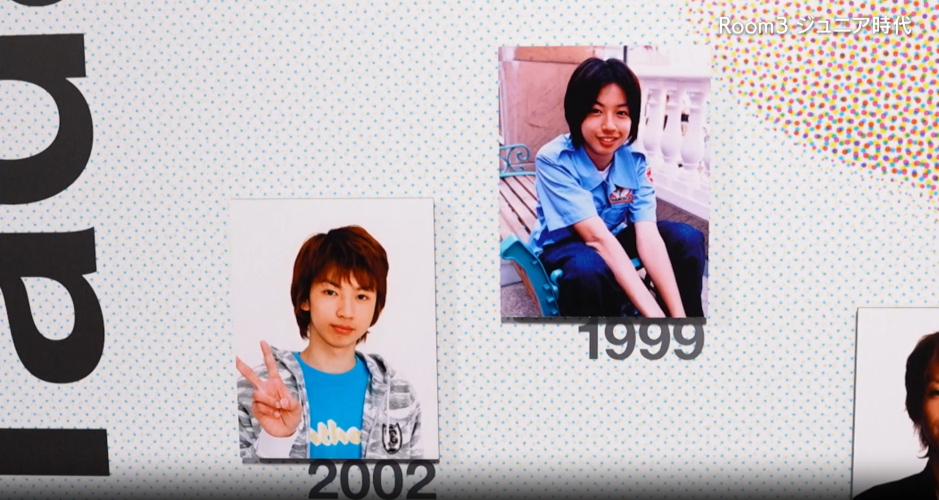 A display featuring two photographs of individuals side by side, one labeled '1999' showing a boy with shoulder-length hair sitting down, and the other labeled '2002' showing a boy giving a peace sign with a short hairstyle, set against a background of patterned paper.