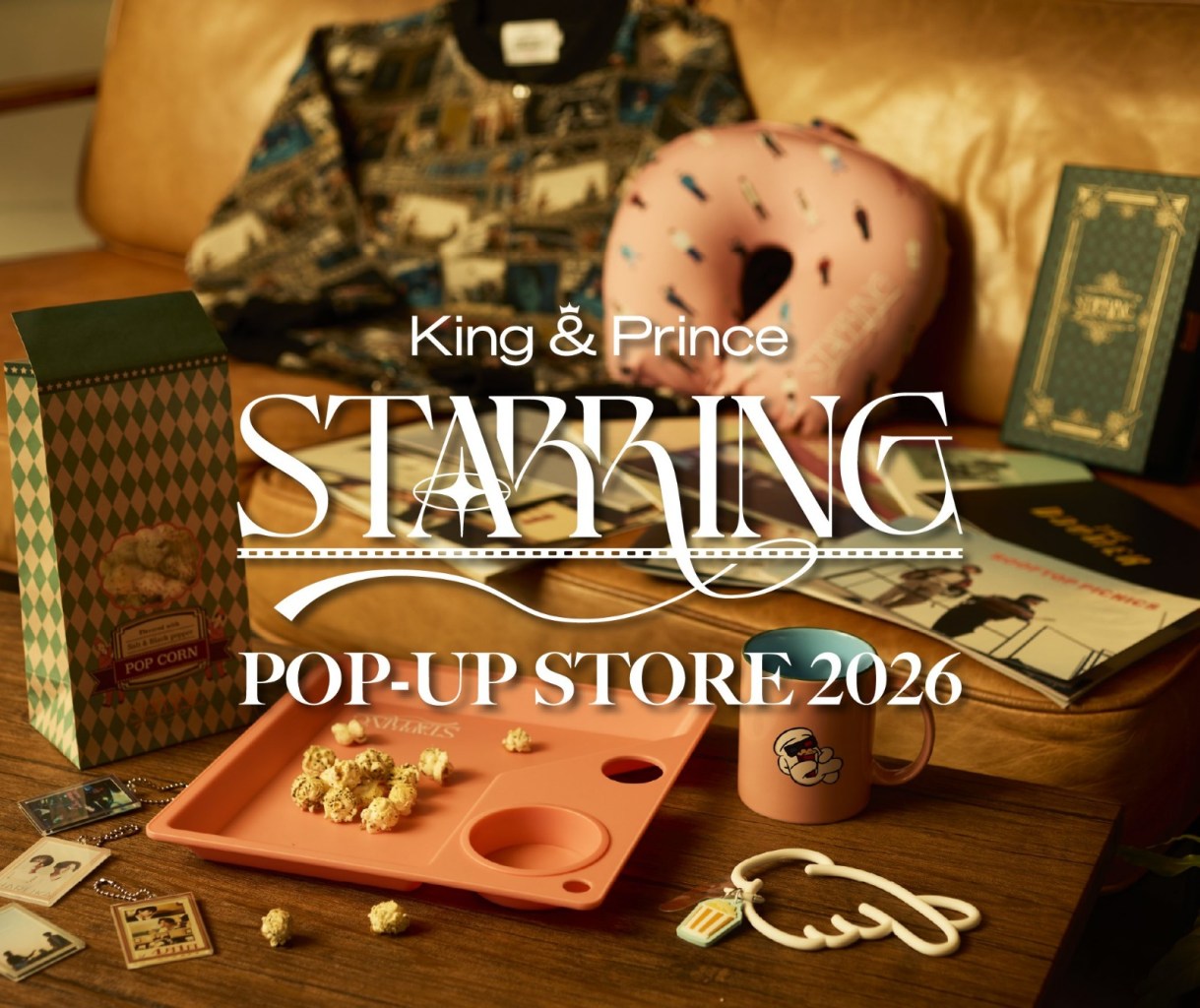 Promotional image for King & Prince's STARRING POP-UP STORE 2026, featuring merchandise including popcorn, a pink donut-shaped pillow, various collectibles, and a colorful mug, set against a wooden background.