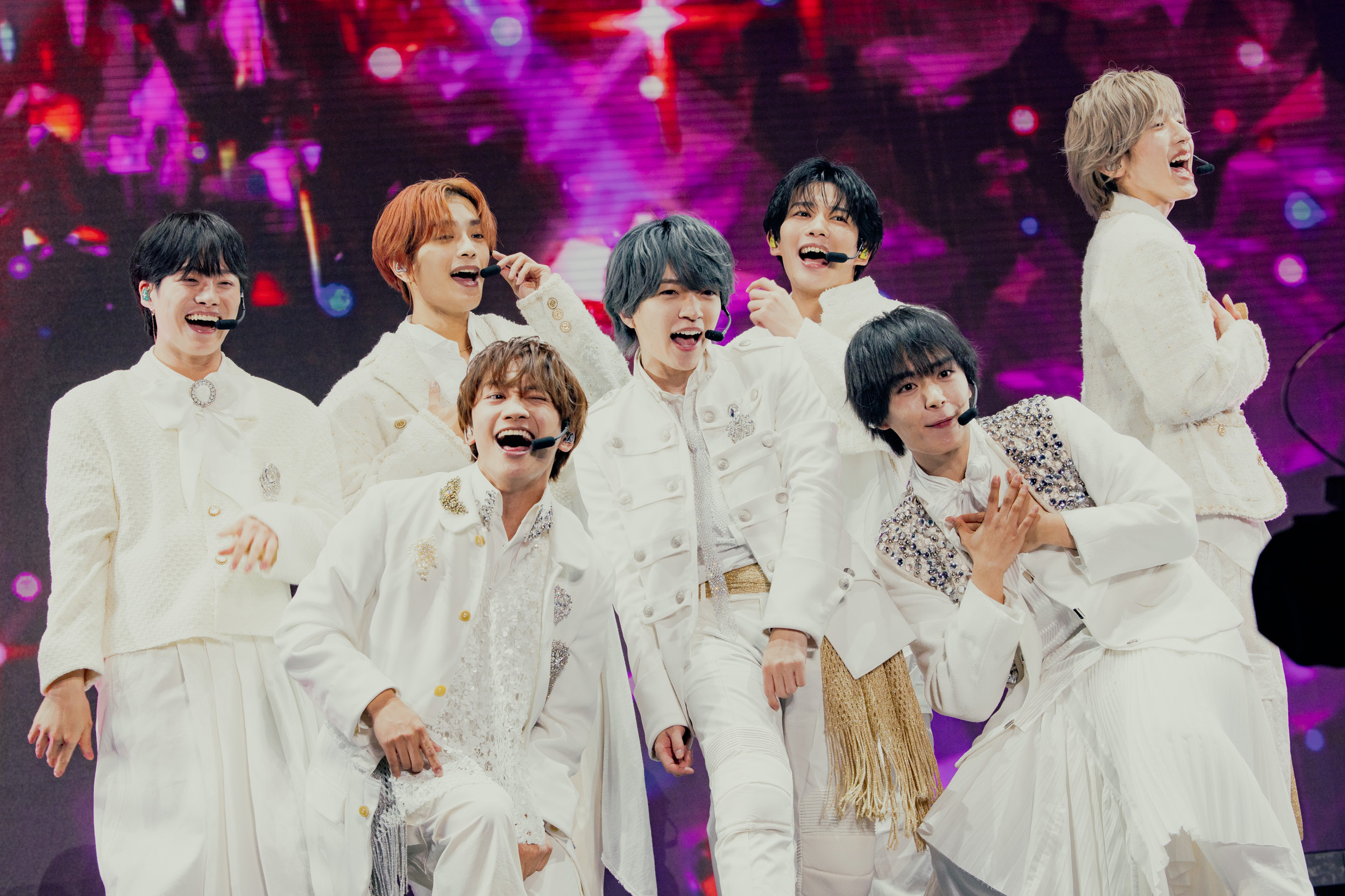 Eight members of Naniwa Danshi performing energetically on stage, dressed in white outfits, smiling and engaging with the audience.