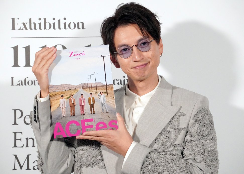 A man holding the cover of the magazine Zessei, featuring a group of individuals on a deserted road, during an exhibition event.