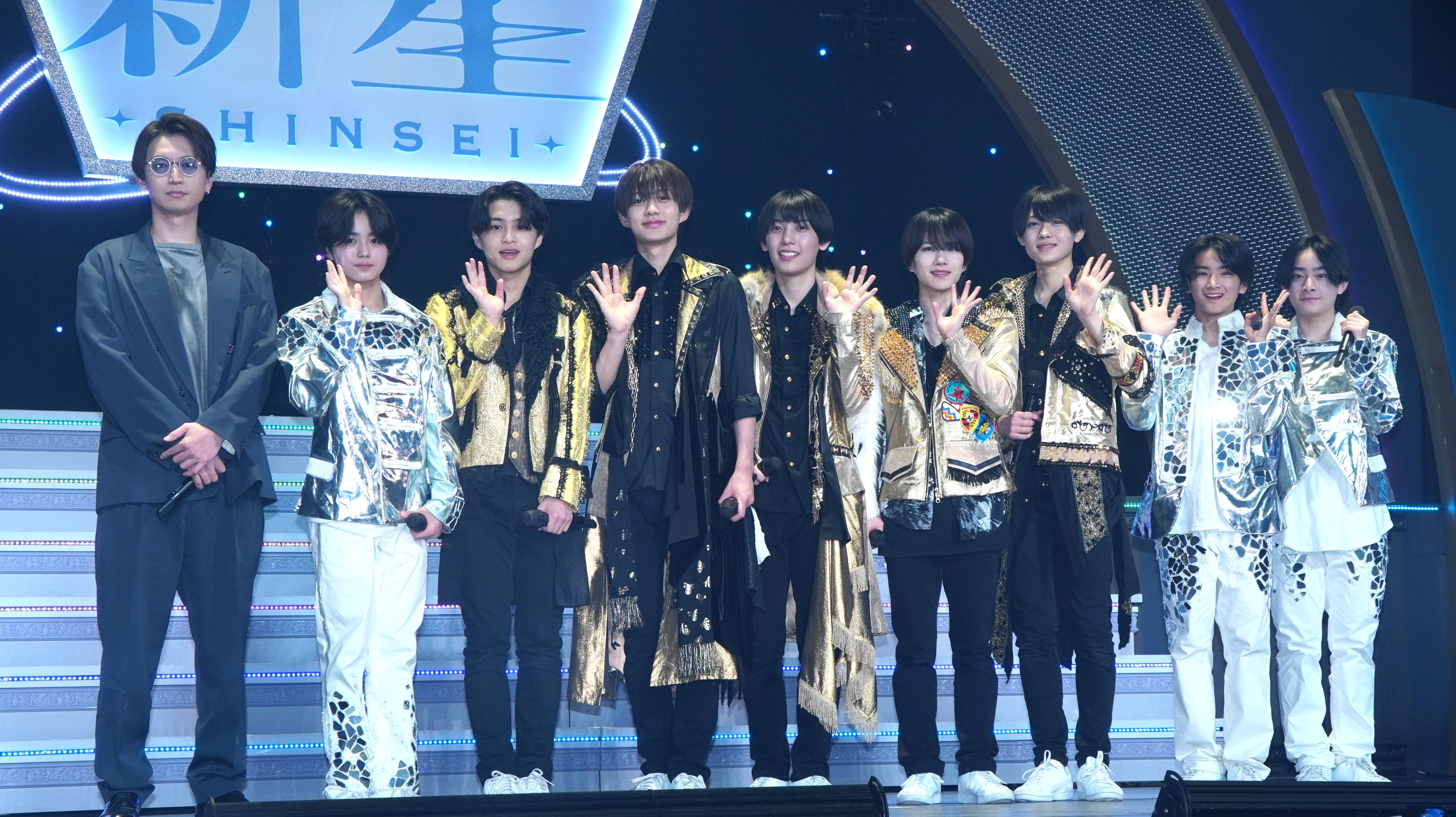 A group of young performers wearing stylish outfits on stage, posing and waving during the _Junior Showcase 2025 SHINSEI_ event.
