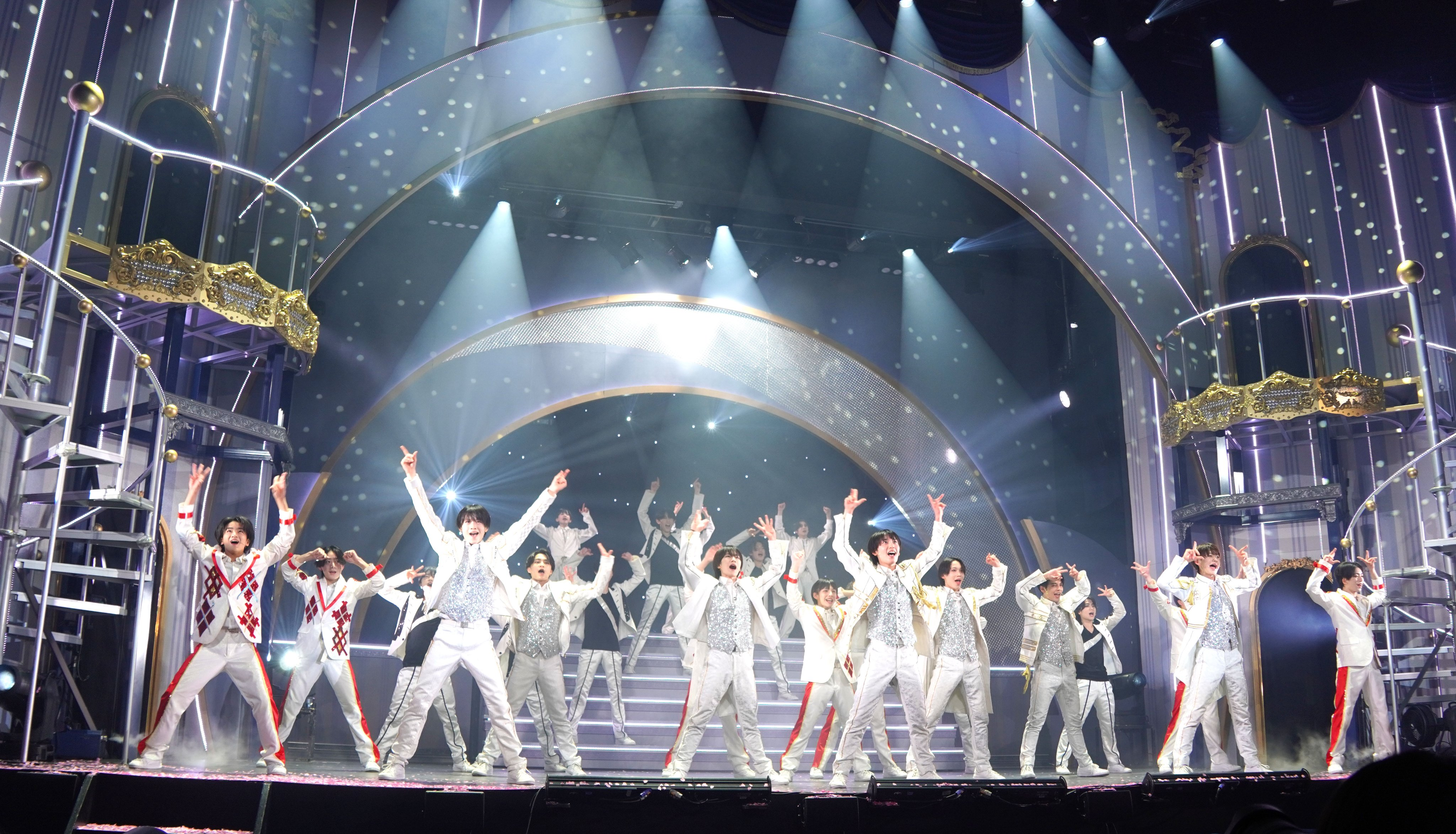 A vibrant performance scene from Junior Showcase 2025 SHINSEI, featuring multiple dancers in sparkling costumes, illuminated by bright stage lights and a glamorous backdrop.