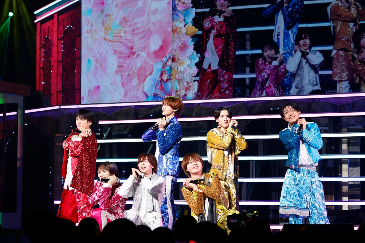 AmBitious performing on stage wearing colorful sparkling costumes with a vibrant backdrop during their nationwide tour.