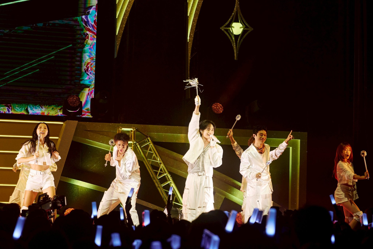 A vibrant concert scene featuring Kento Nakajima and backup performers dressed in white outfits, engaging with an enthusiastic audience holding glowing light sticks.