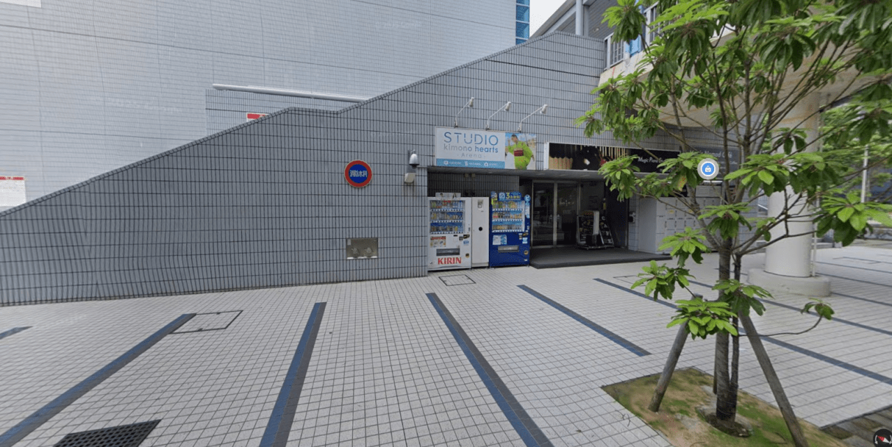 Exterior view of the Studio Kimono Hearts building at Yokohama Arena, featuring a vending machine and greenery in the foreground.