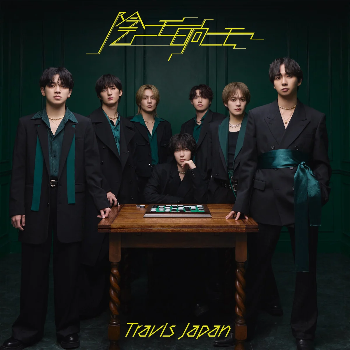 A group of seven men posing for a photo in stylish black suits with teal accents, standing together around a wooden table with a game board on it. The background is a dark green color, adding to the dramatic atmosphere.