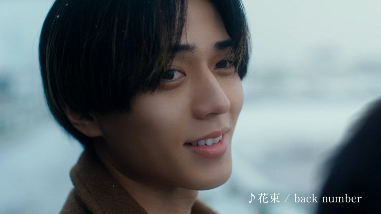 Close-up portrait of a young man with straight black hair, smiling softly against a snowy background.