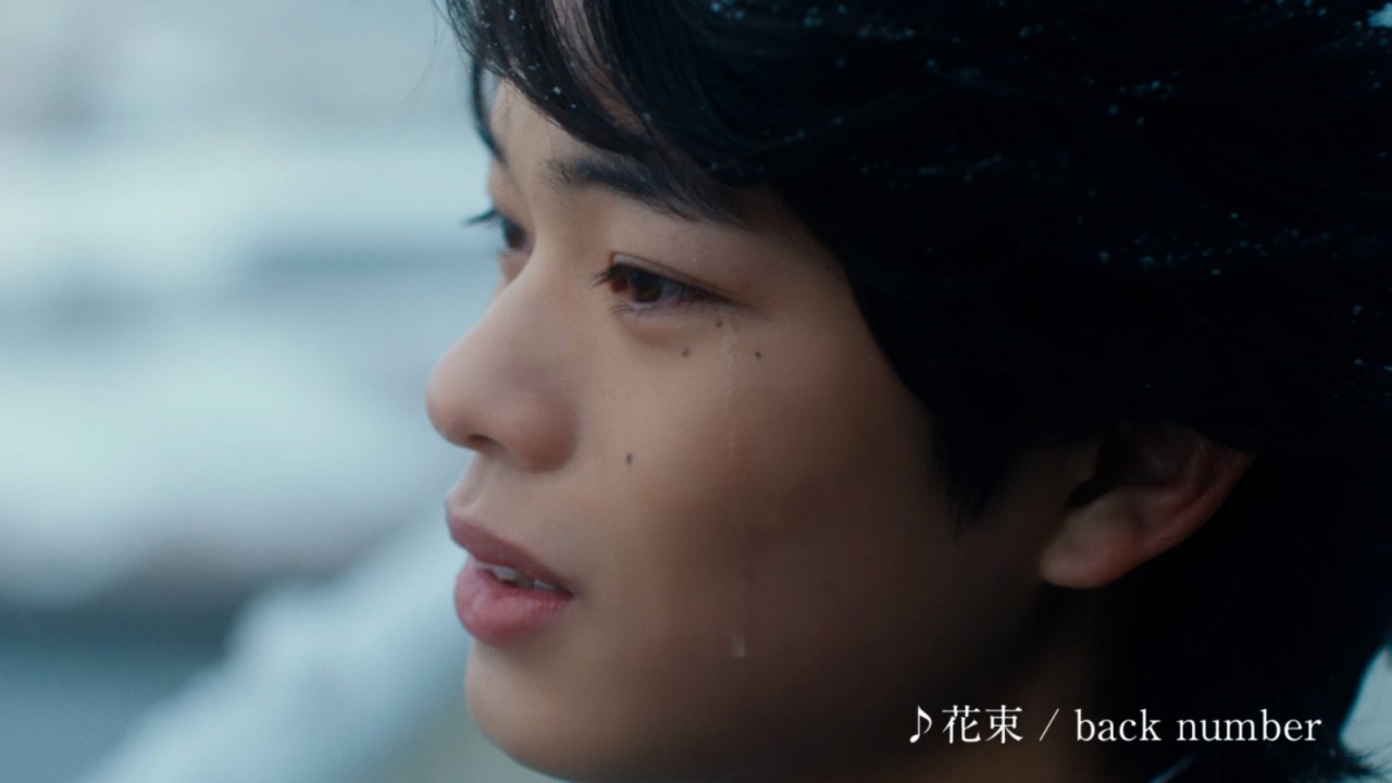 Close-up profile of a young man with tear-streaked cheeks, looking contemplatively to the side, against a blurred background.