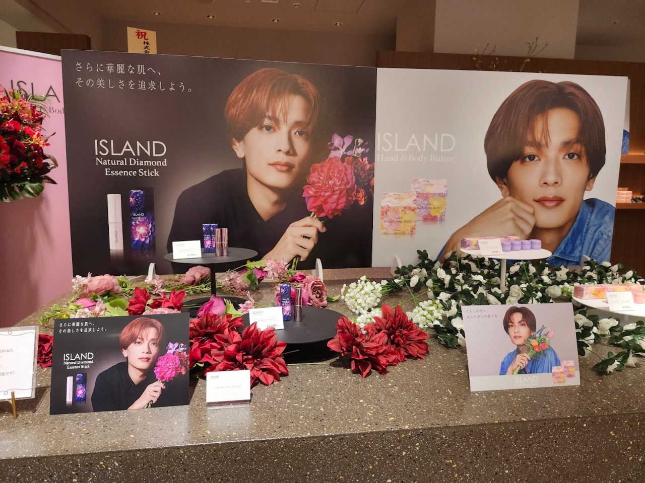 Display featuring ISLAND brand products including Natural Diamond Essence Stick and Hand & Body Butter, with promotional images of a male model holding flowers.