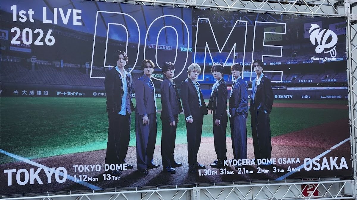 A promotional banner for a live concert titled '1st LIVE 2026', featuring seven individuals in stylish outfits standing together on a baseball field. The banner includes text with concert dates for TOKYO DOME and KYOCERA DOME OSAKA.