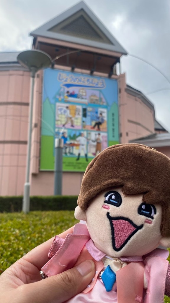 A person holding a plush toy in front of a colorful building with a large sign depicting various activities.