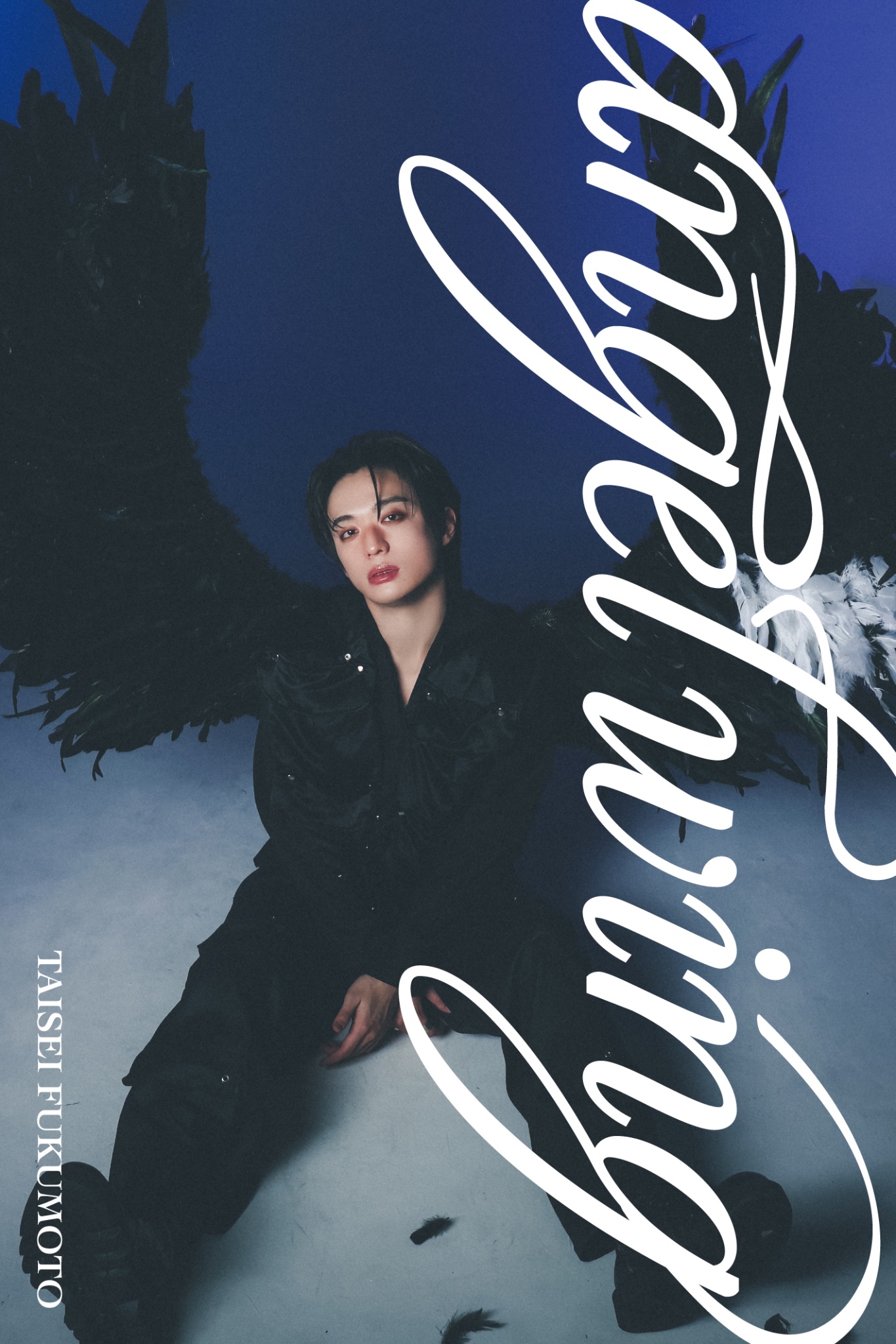 A model seated on the floor, wearing dark clothing, with large black wings extending behind. The background is a gradient of blue, and the word 'angelwing' is artistically displayed in white across the image.