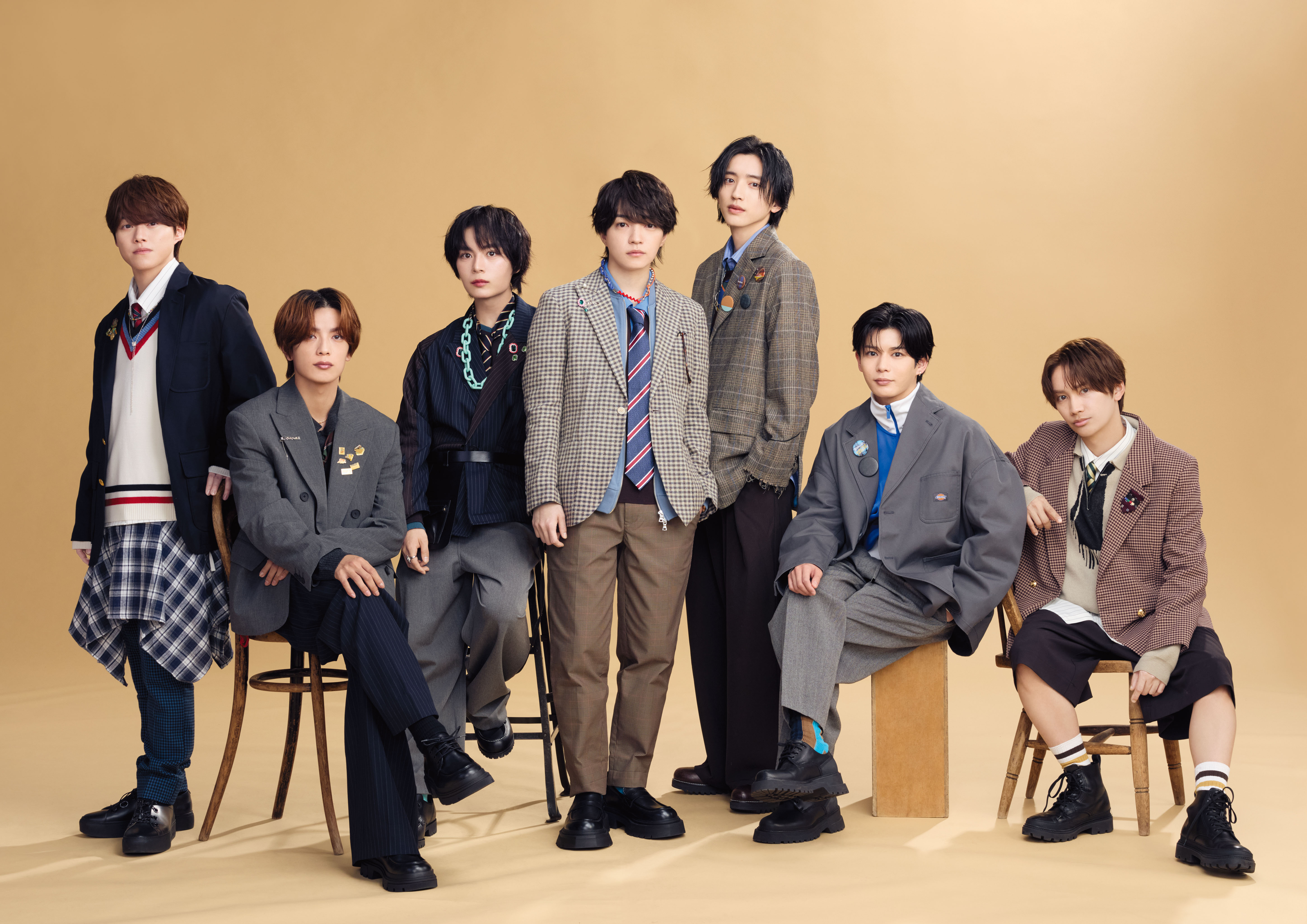 A group photo of eight individuals posing together against a beige background. They are dressed in various stylish outfits, including blazers, plaid patterns, and casual wear. Some are seated on chairs, while others stand beside them, exhibiting a friendly and fashionable demeanor.