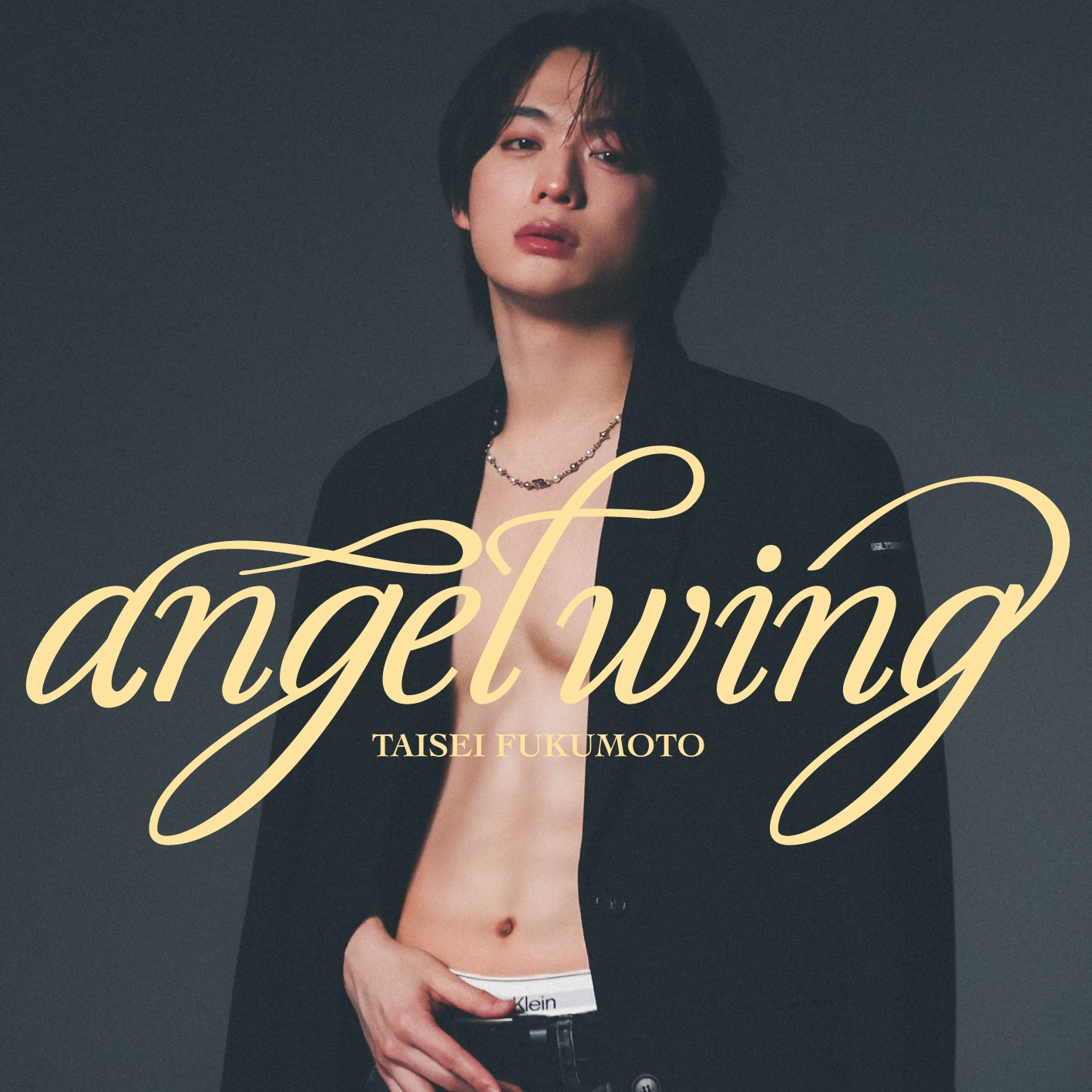 A young man with shoulder-length dark hair and a neutral expression poses in a half-open blazer, revealing his torso. He wears a necklace and stands against a dark background, with the words 'angel wing' and 'TAISEI FUKUMOTO' artistically displayed.