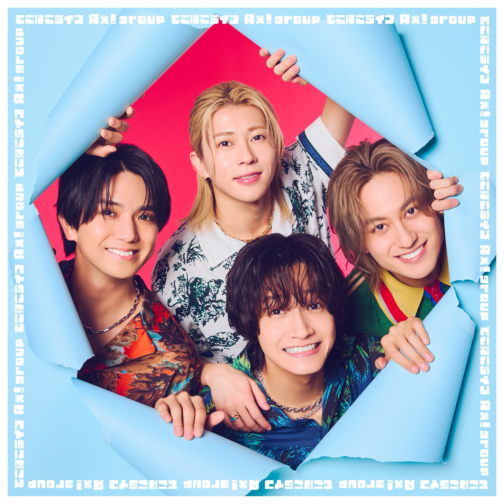 A group of four young men smiling and posing together while framed by torn blue paper. They have stylish haircuts and colorful outfits, with a bright red background.