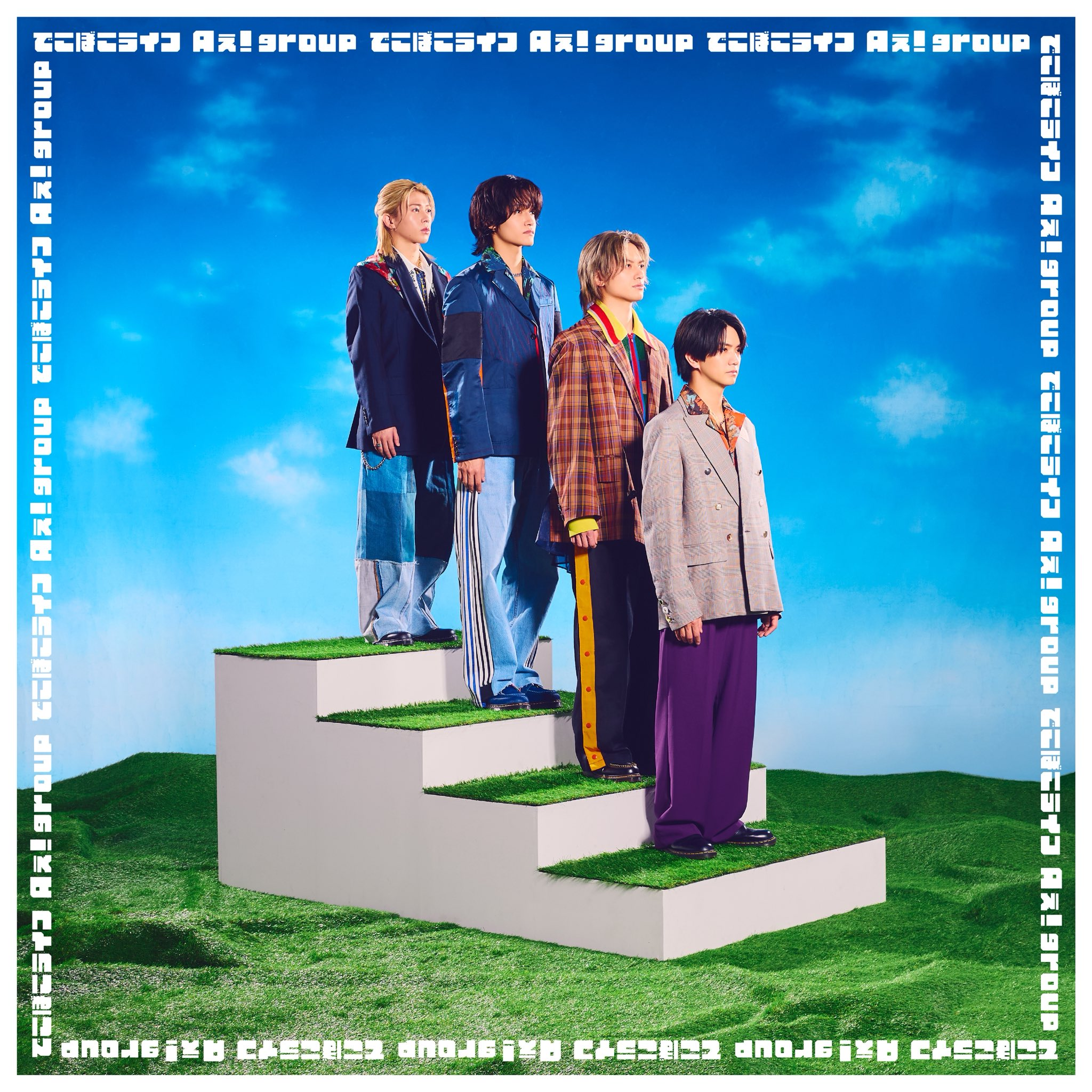 Four individuals standing on a grass-covered staircase against a blue sky, dressed in stylish, contemporary outfits.
