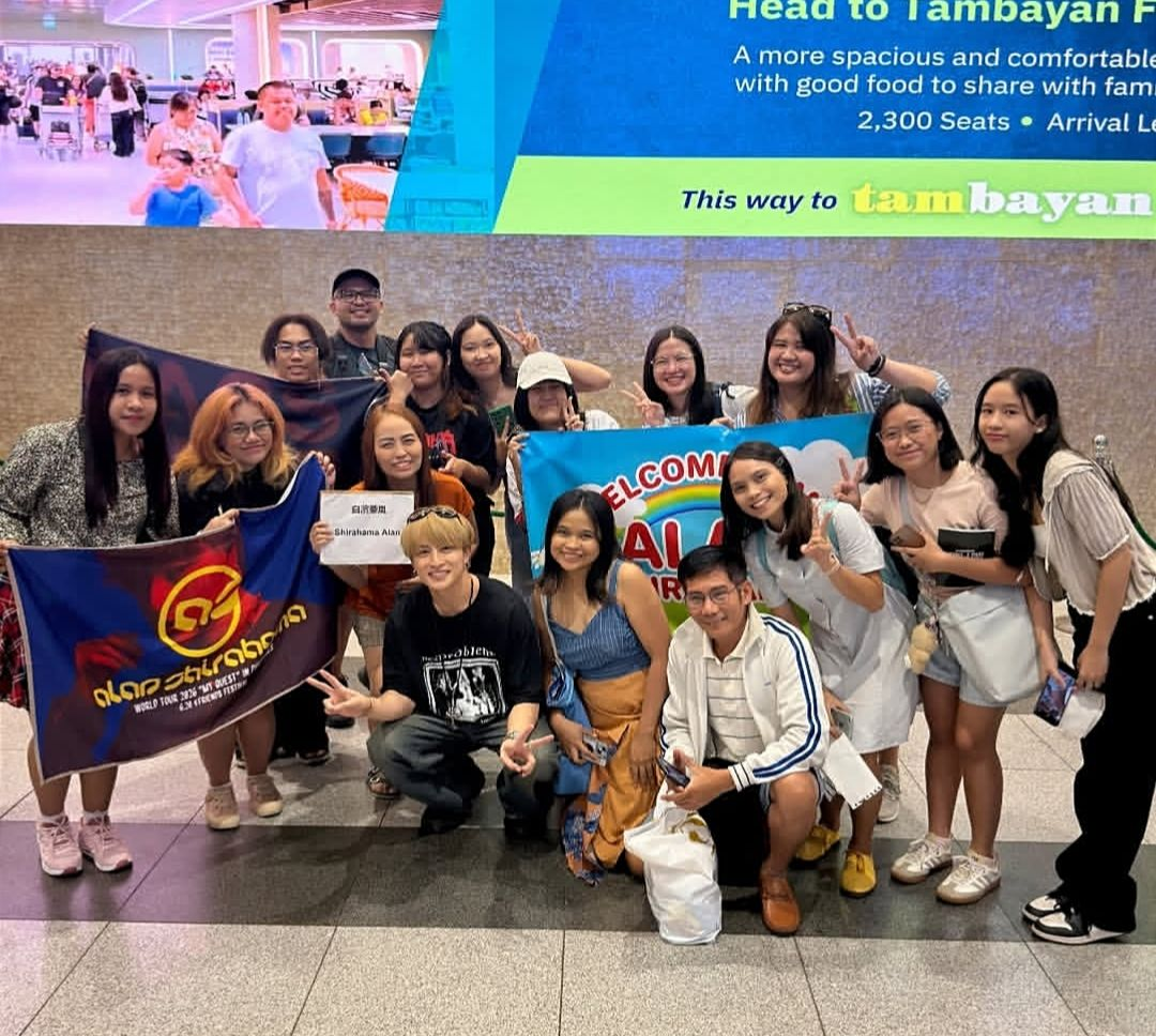 Group photo of a diverse group of friends smiling and posing together at an airport welcome area, holding banners and signs.