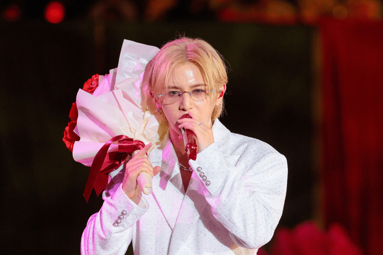 A singer wearing a white beaded outfit and glasses, holding a bouquet of flowers while performing on stage.