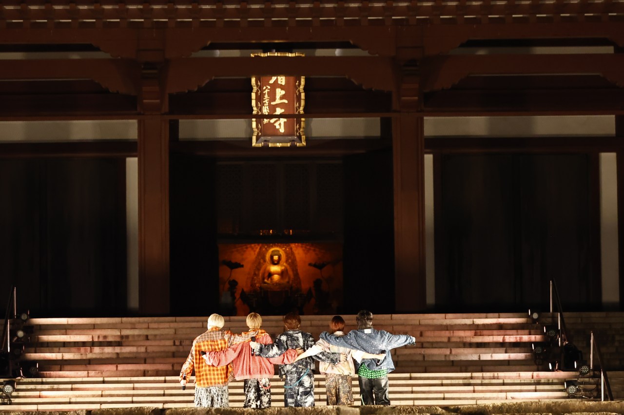 Five individuals standing together with their arms around each other's shoulders, facing a large illuminated statue in a traditional temple setting.